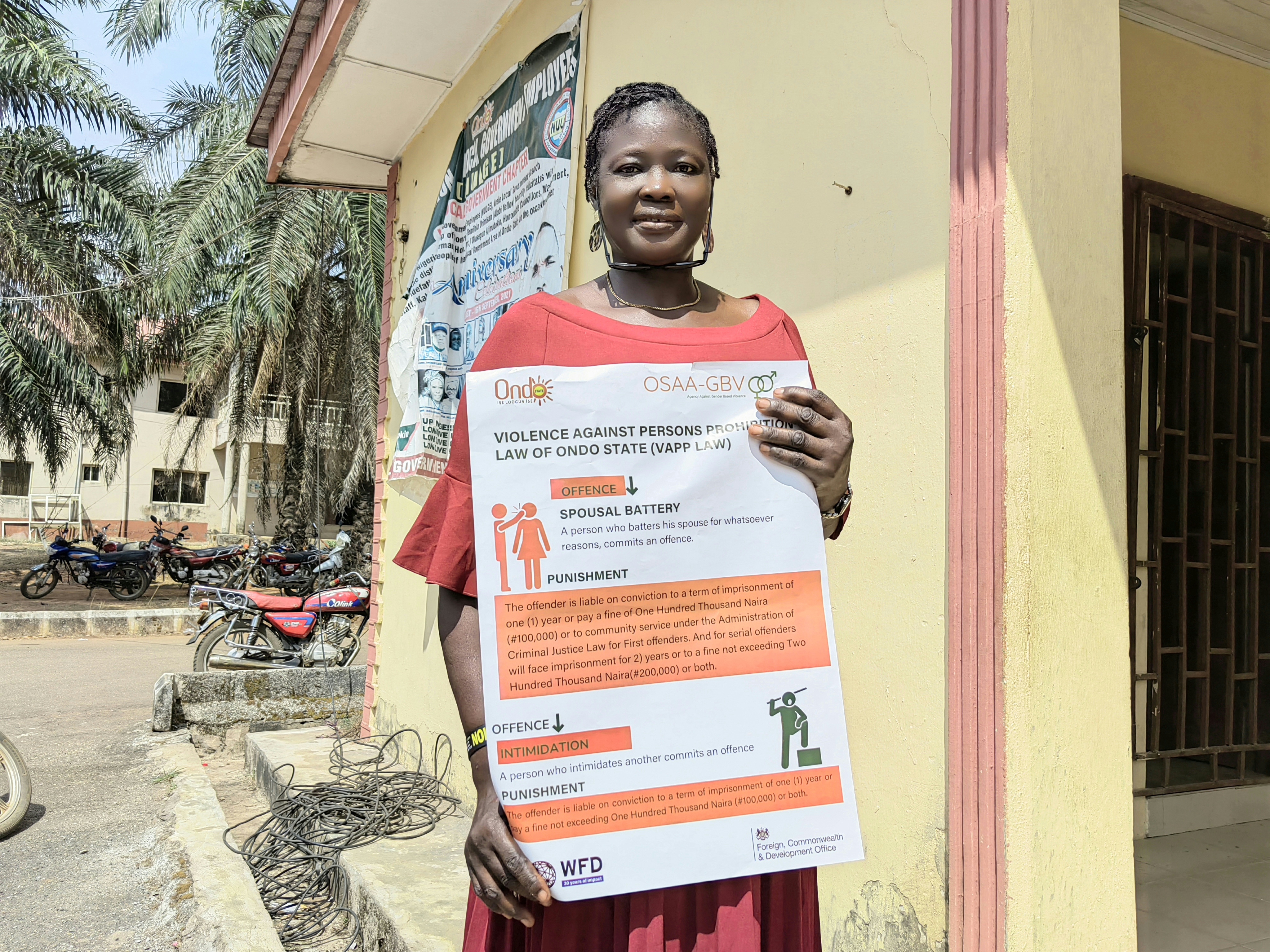 A woman standing outside a building holds an awareness raising poster produced with support by WFD