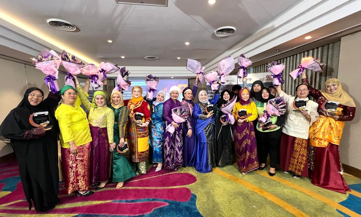 A group of women smiling and holding bunches of flowers in the air