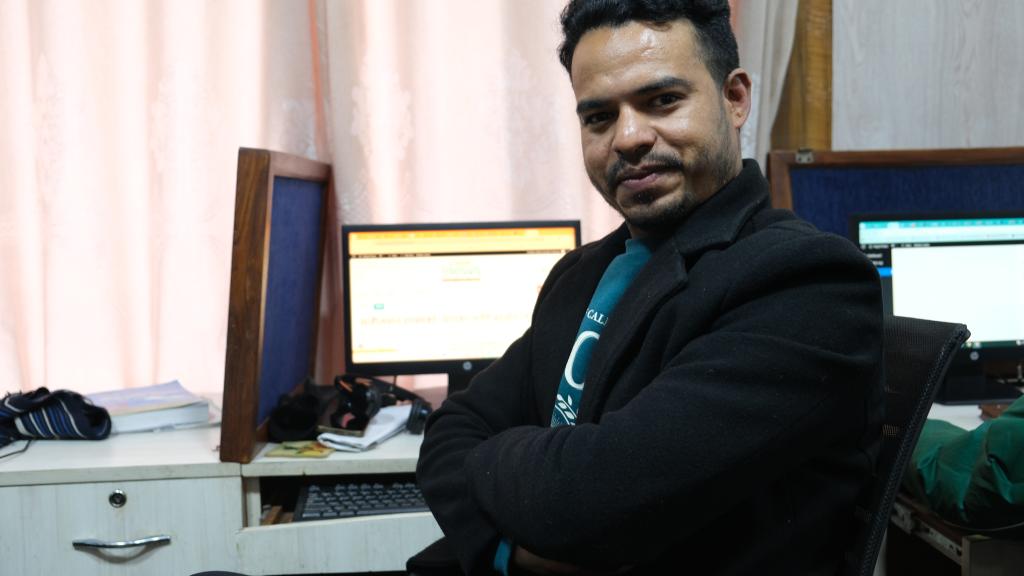 A man sitting in front of a computer screen that says "Nepal Views"