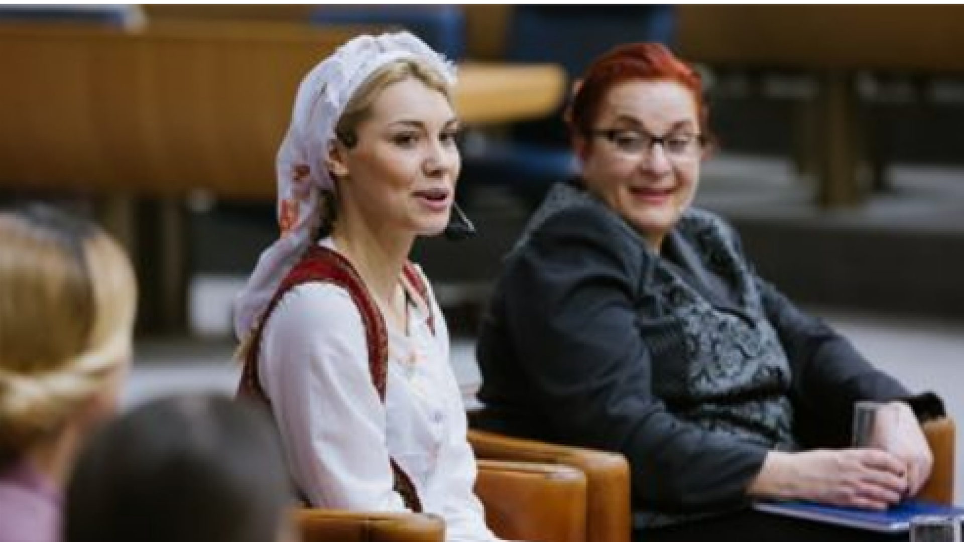 two women sitting next to each other, smiling and speaking